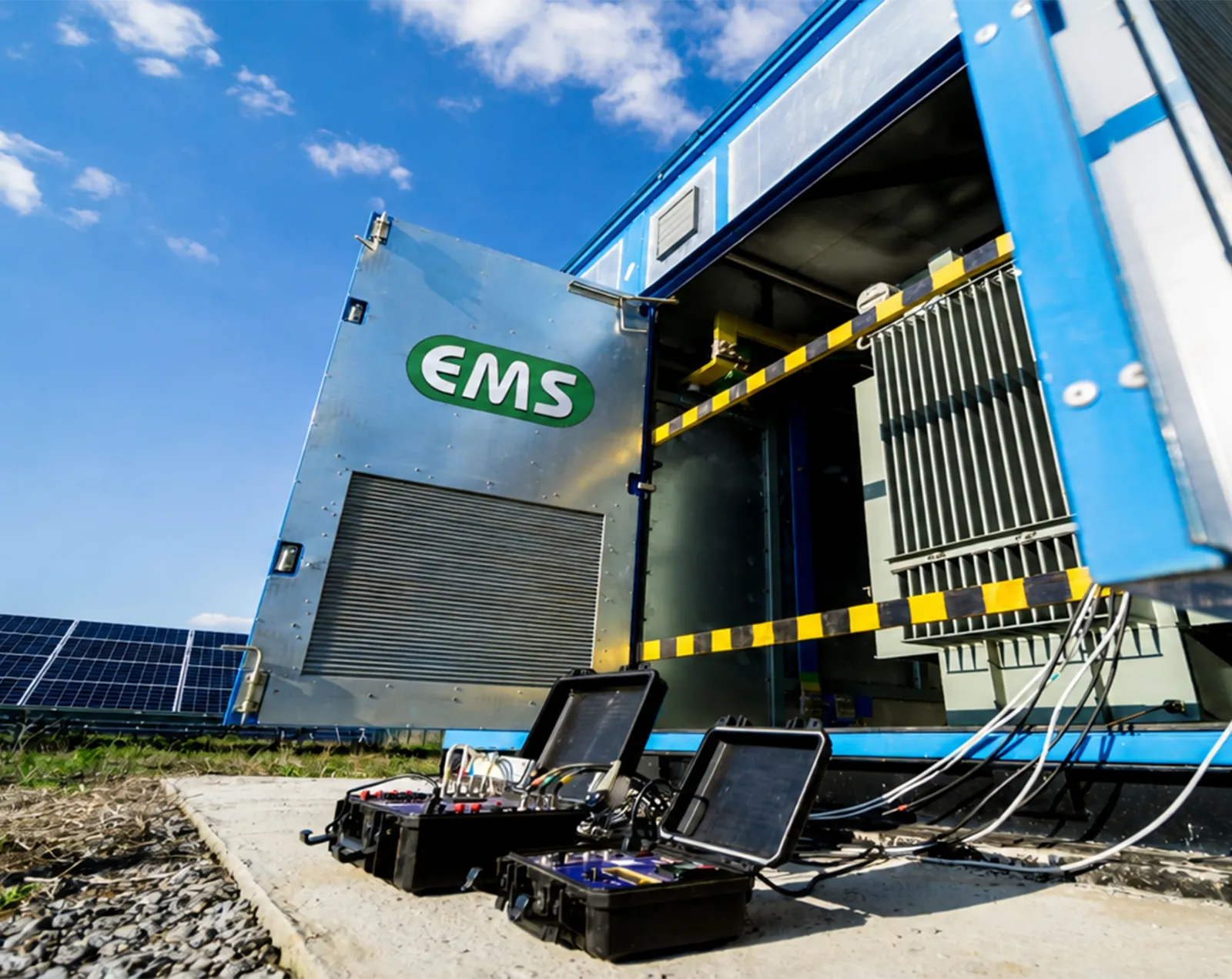 Open EMS energy storage container with test equipment beside a solar array